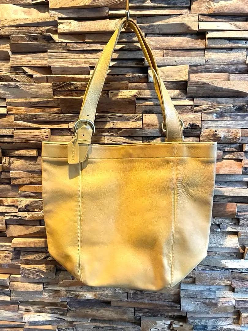 Yellow Old Coach cow leather tote bag hanging against a wood wall.