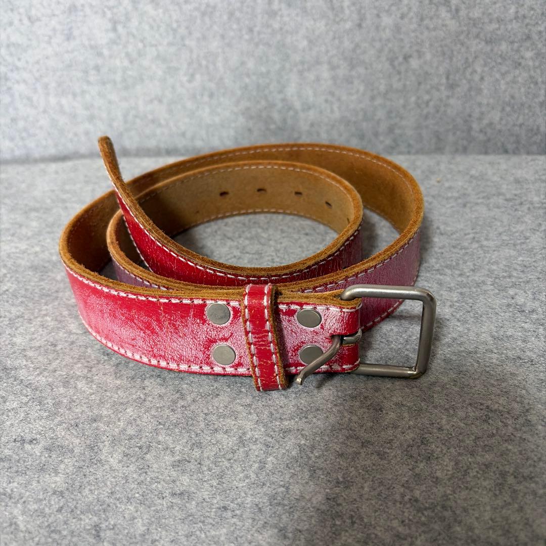 Coiled red leather belt with white stitching and a metal buckle on a gray surface.