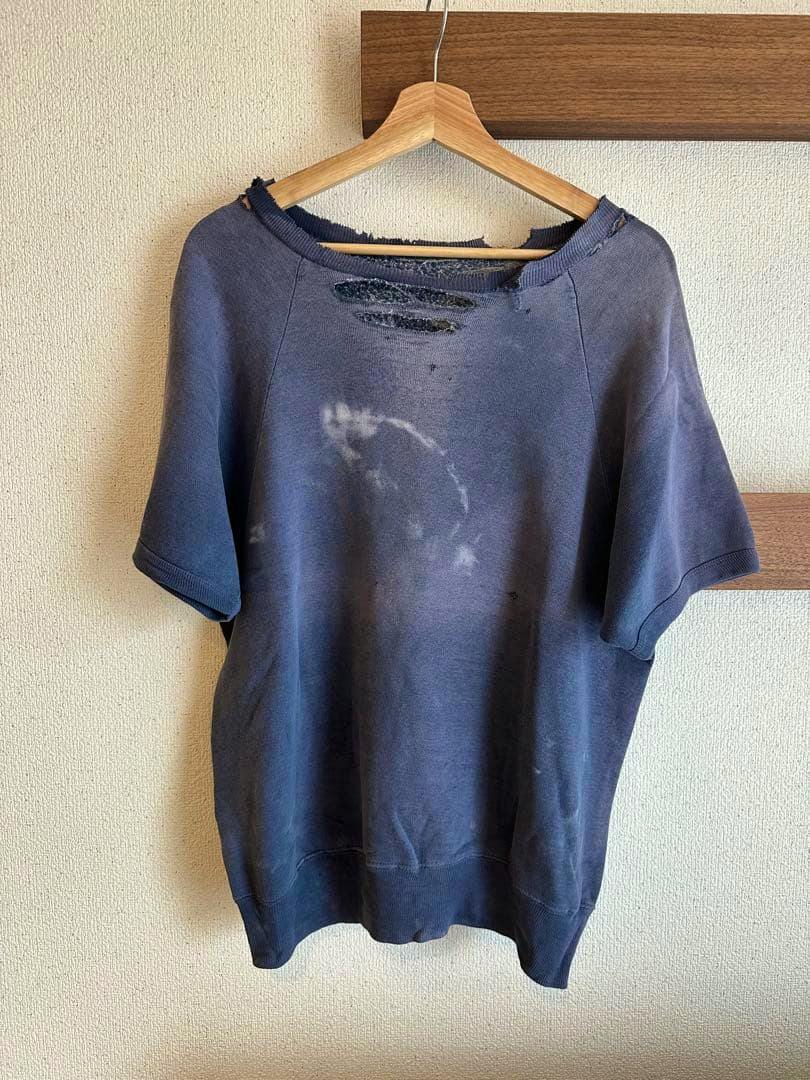 Front view of a vintage cutoff navy cotton sweatshirt with a distressed neckline and light bleach marks, hanging on a wooden hanger.