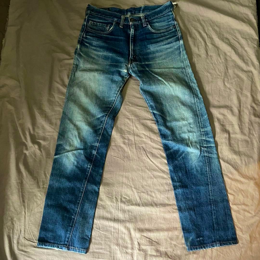 Front of a pair of men's blue denim jeans laid flat showing fading, whiskering, and creases.