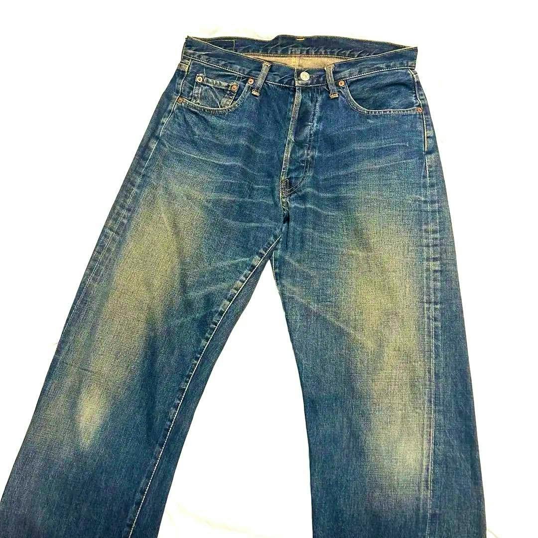 Front view of men's blue denim jeans laid flat showing front pockets, a visible button waist, and faded whiskering on the thighs.