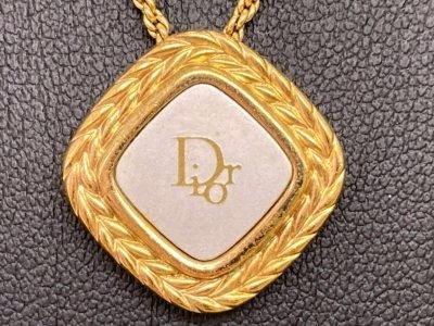 Close-up of a gold-tone diamond-shaped necklace pendant with a white square center printed with the Dior logo.