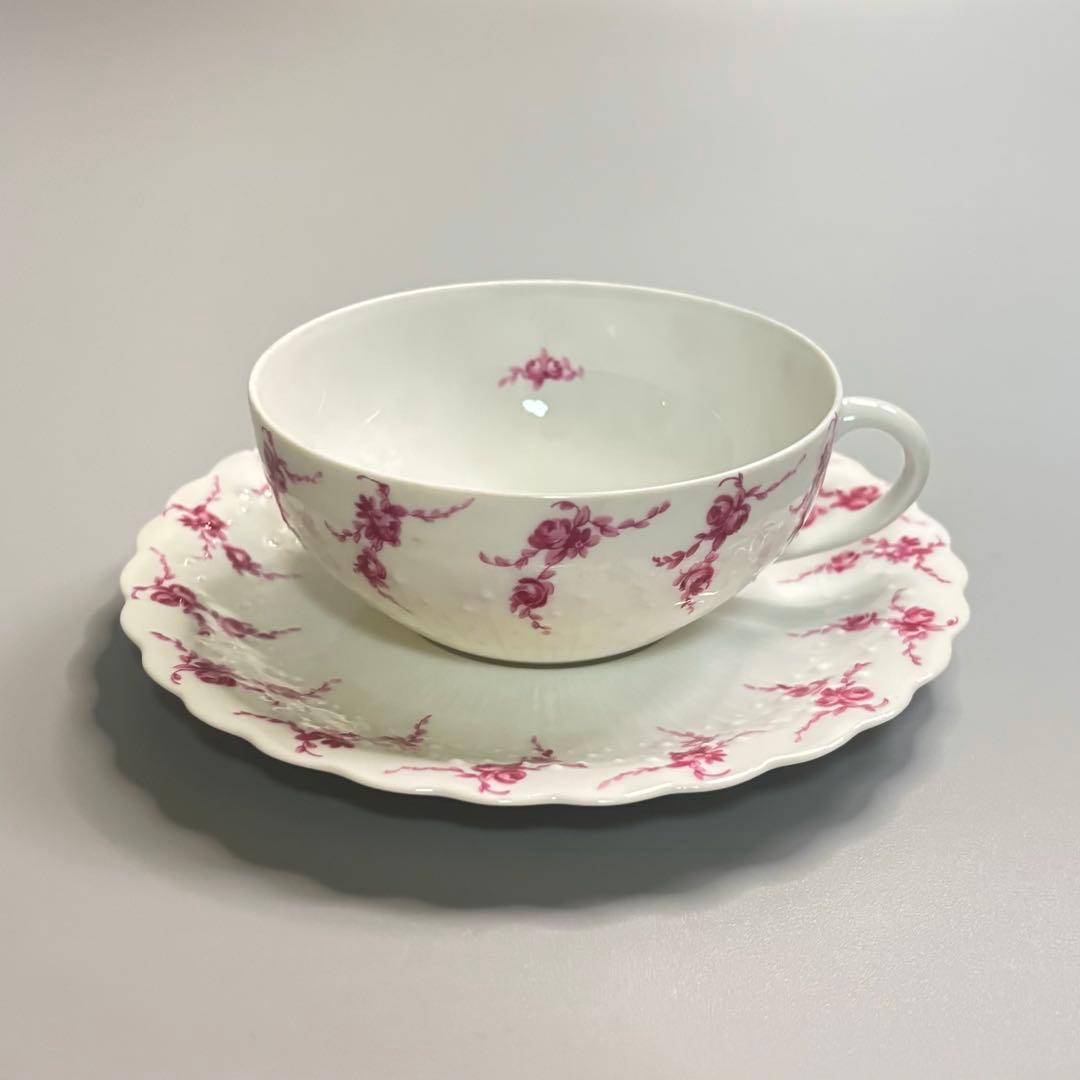 Porcelain cup and matching saucer with pink rose decoration photographed on a gray surface.