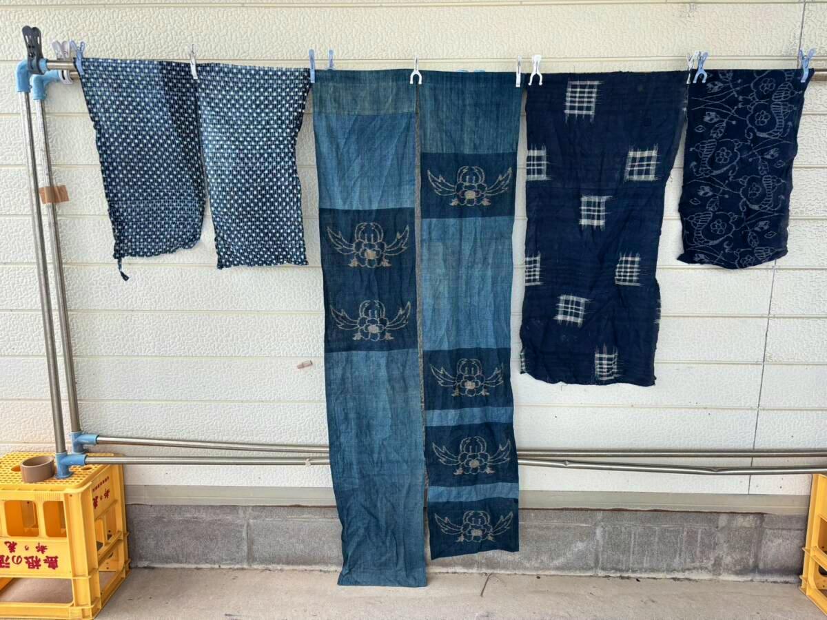 Indigo-dyed cotton fabric pieces and strips with kasuri-style patterns hanging on a rod against a wall.