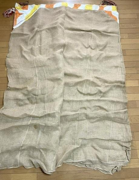 Vintage hemp mosquito net with a colored top edge and tassels spread out on a wooden floor.