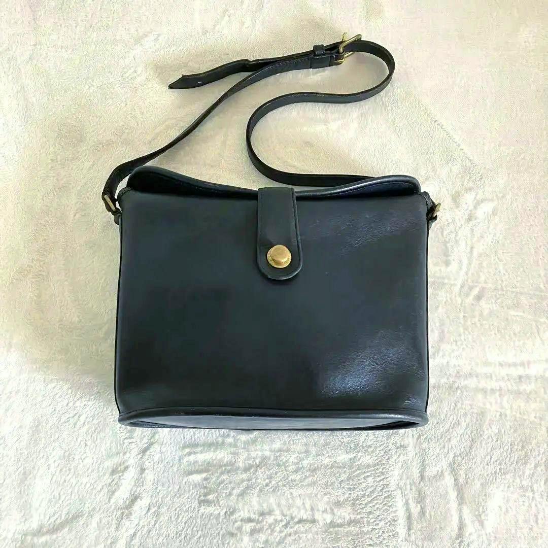 Black cow leather Old Coach shoulder bag with a flap and brass snap closure on a light background.
