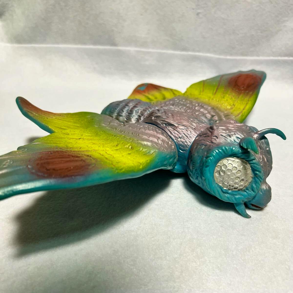 Colorful Marusan Mothra soft vinyl figure shown lying on a white surface, visible wings and textured head.