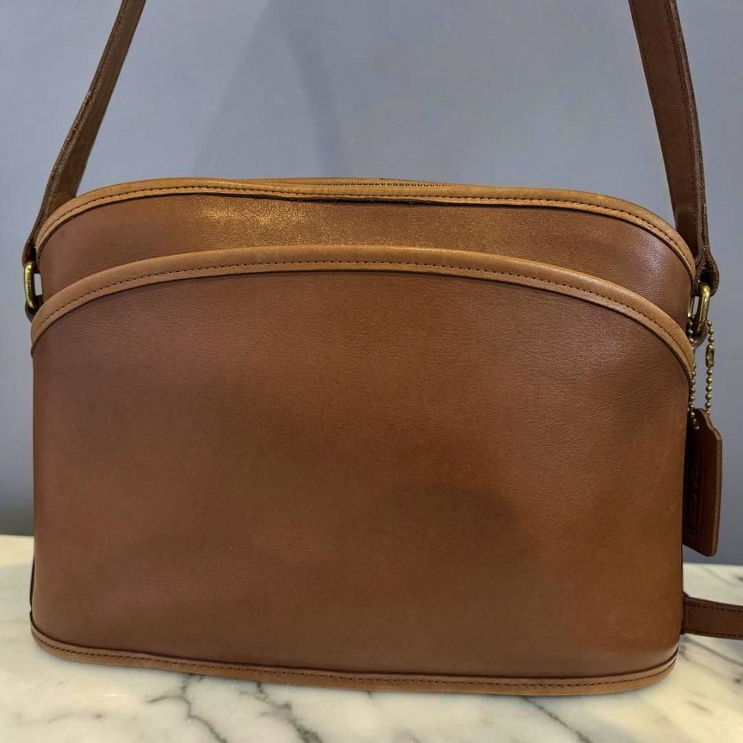 Front view of a brown Coach leather shoulder bag placed on a marble surface.