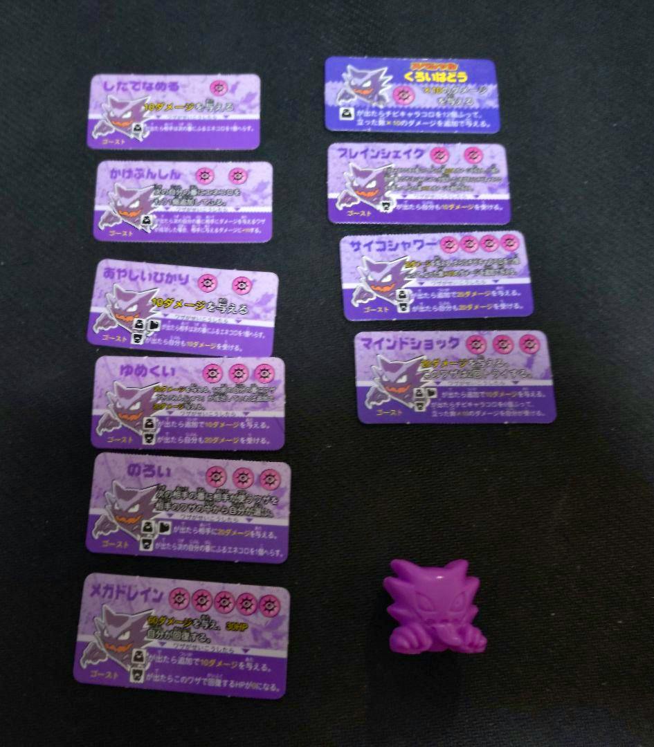 A small purple plastic ghost figure on a black surface next to multiple purple rectangular cards with Japanese text and a ghost illustration.
