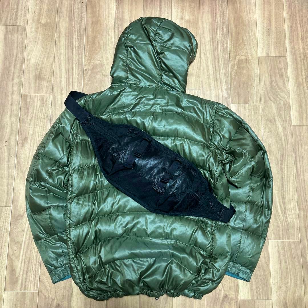 A black Porter shoulder/sling bag laid flat on a green puffer jacket on a wooden floor.