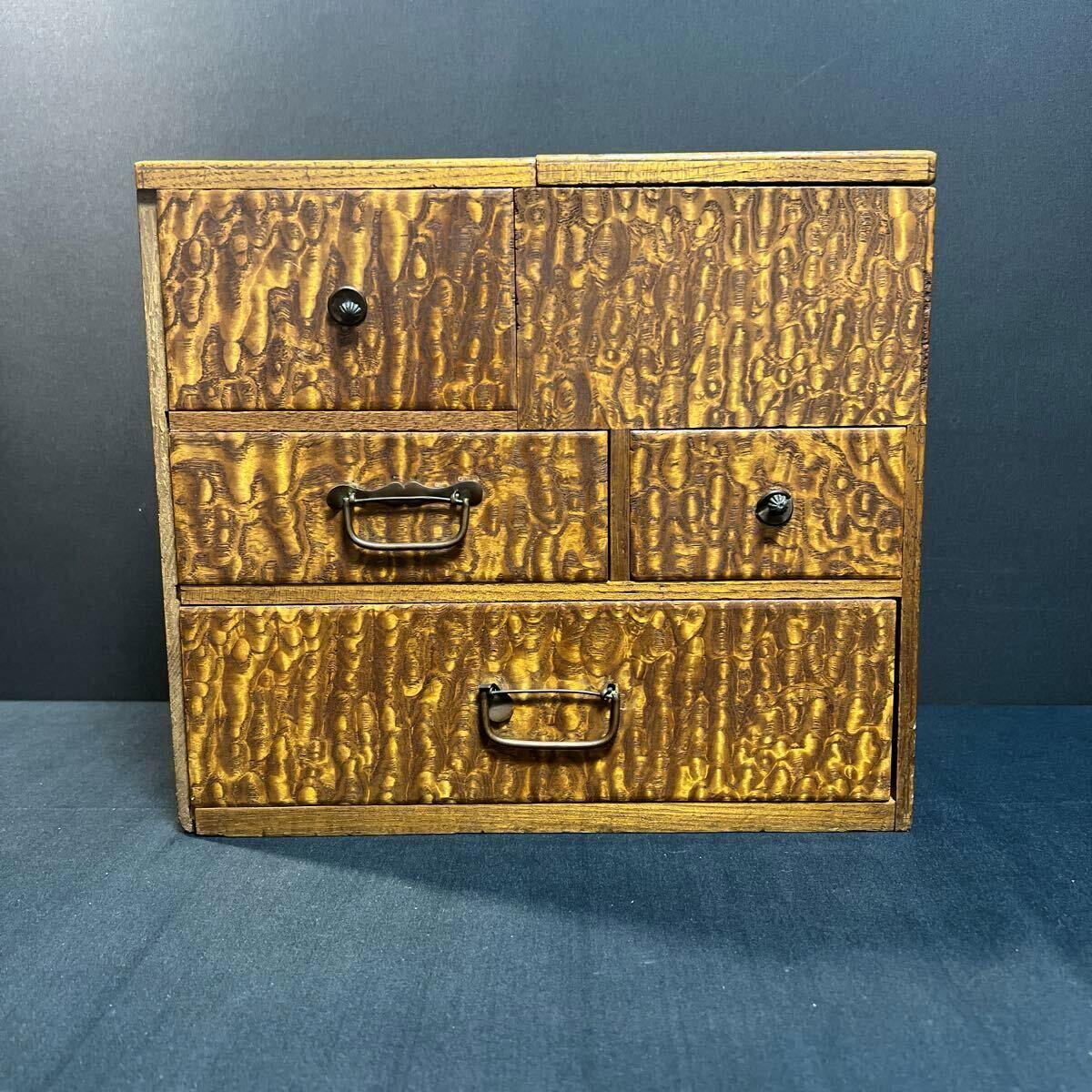 Front view of a wooden sewing box with multiple drawers and a figured tama-moku wood grain finish against a dark background.