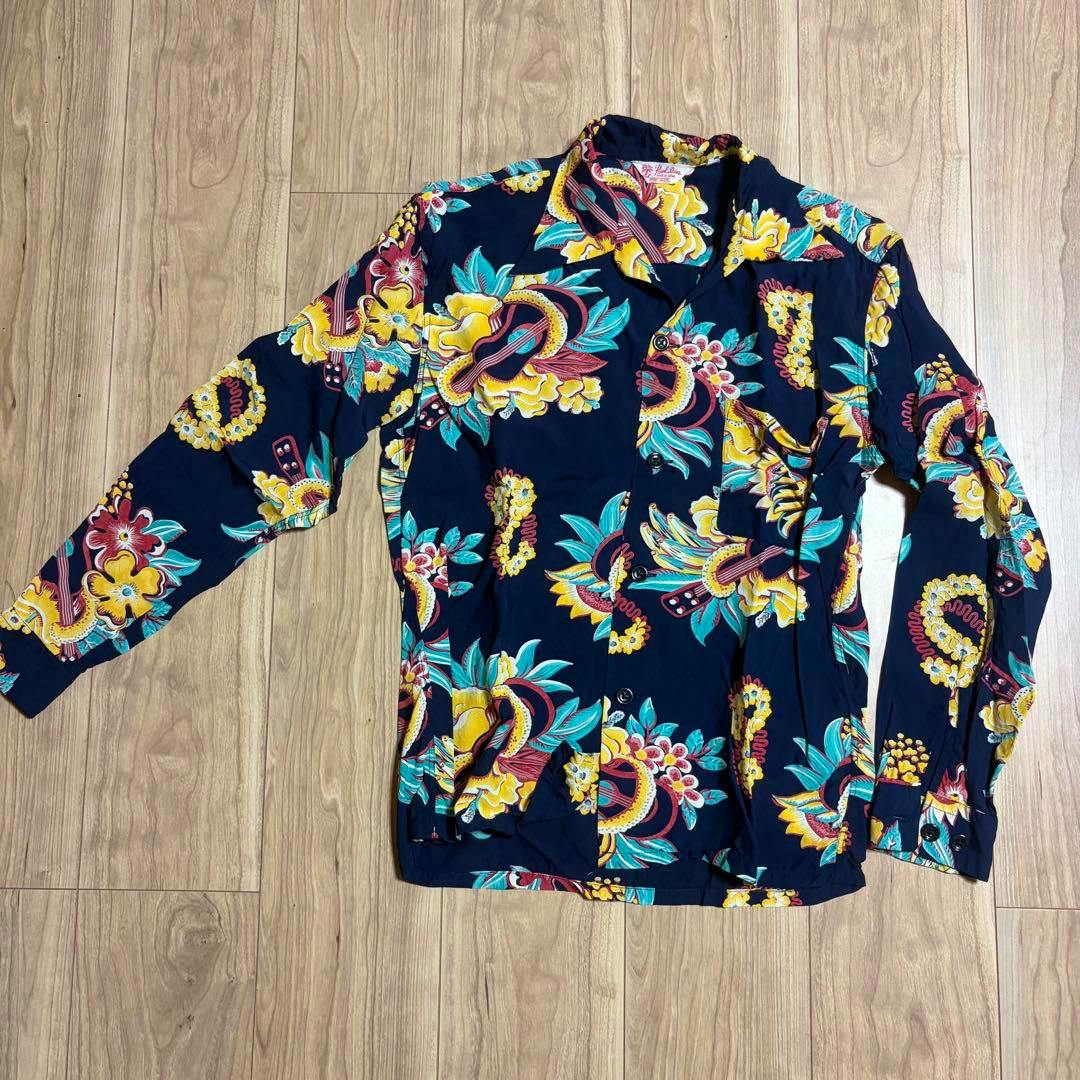 Navy vintage-style long-sleeve Aloha shirt with multicolored floral pattern laid flat on a wooden floor.