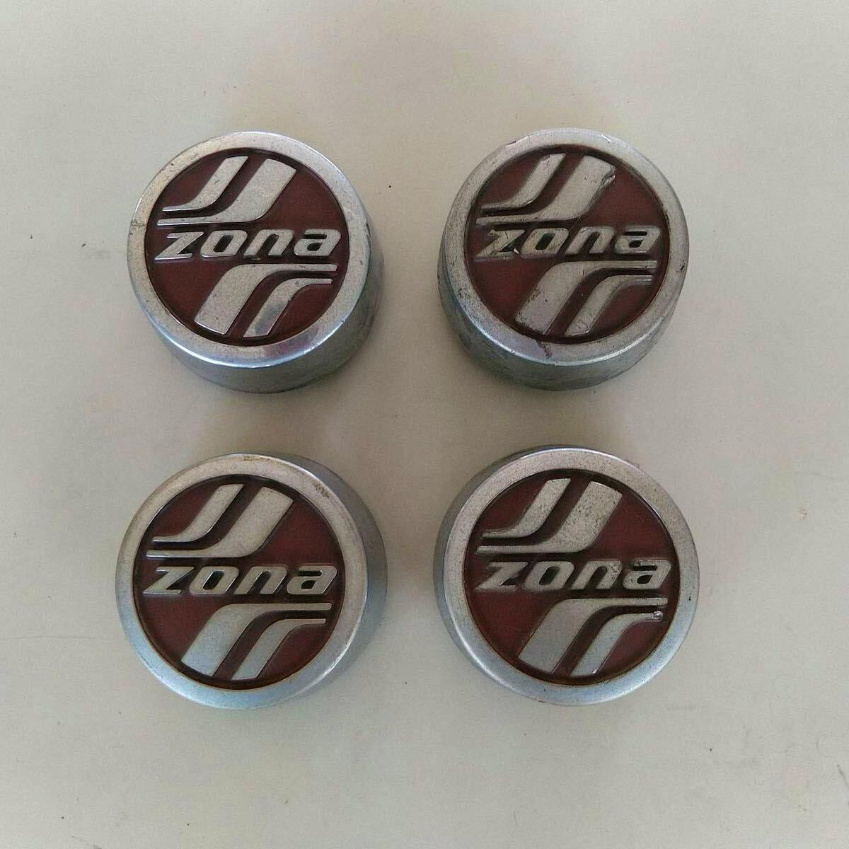 Four ZONA car wheel center caps arranged in a square on a light surface, showing the ZONA logo.