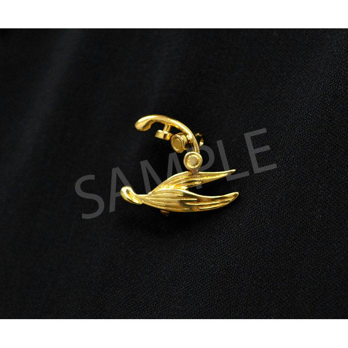 Gold metal pin in a stylized wing motif photographed on black fabric.