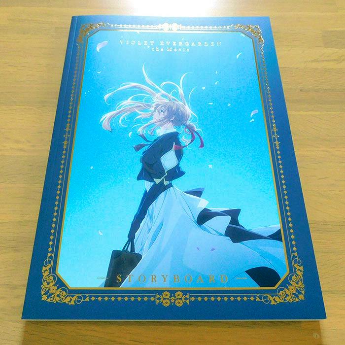 Photograph of the Violet Evergarden storyboard illustration book showing its blue cover art with the character standing and holding a bag.