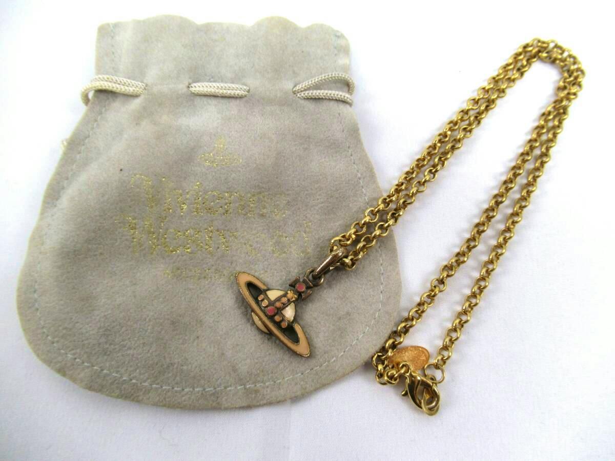 A gold-tone Vivienne Westwood orb pendant necklace with a gold chain laid on a gray Vivienne Westwood drawstring pouch.
