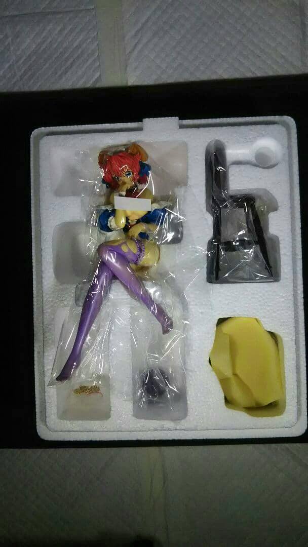 Pre-painted plastic figure of 向坂 つぼみ seated in styrofoam packaging, wrapped in plastic with the base and parts visible.