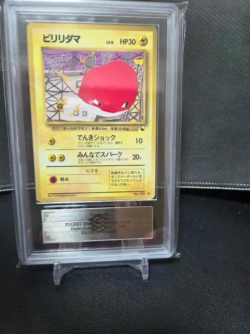 Front view of the Japanese Voltorb trading card in a clear protective slab, showing the card artwork and a metal nameplate below.