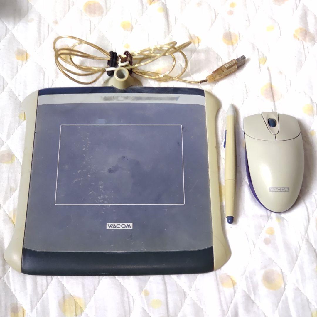 Wacom FAVO ET-0405A-U USB pen tablet with its stylus, coiled USB cable, and a computer mouse on a quilted surface.