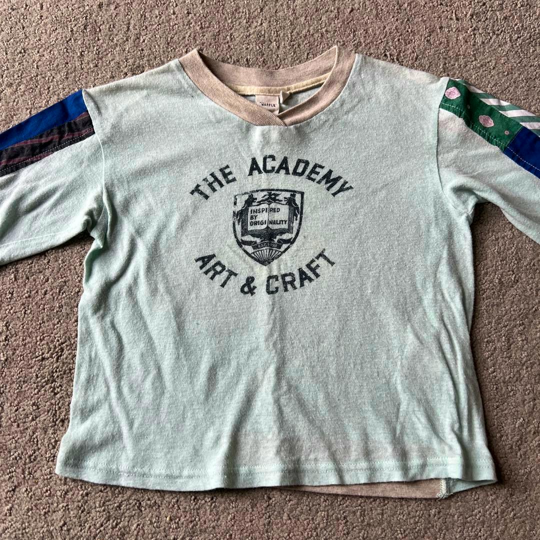 Laid-flat children's long-sleeve cotton shirt (size S) pale green with a printed "THE ACADEMY ART & CRAFT" crest and contrasting patterned sleeve panels.