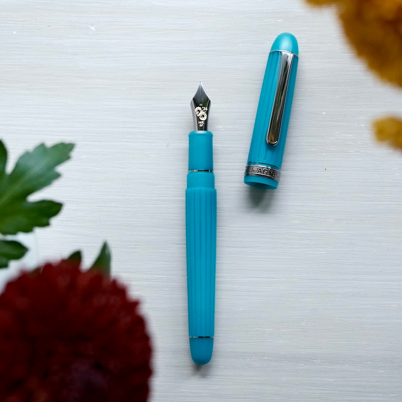 An azure-turquoise fountain pen shown uncapped with the cap placed beside it on a light background.