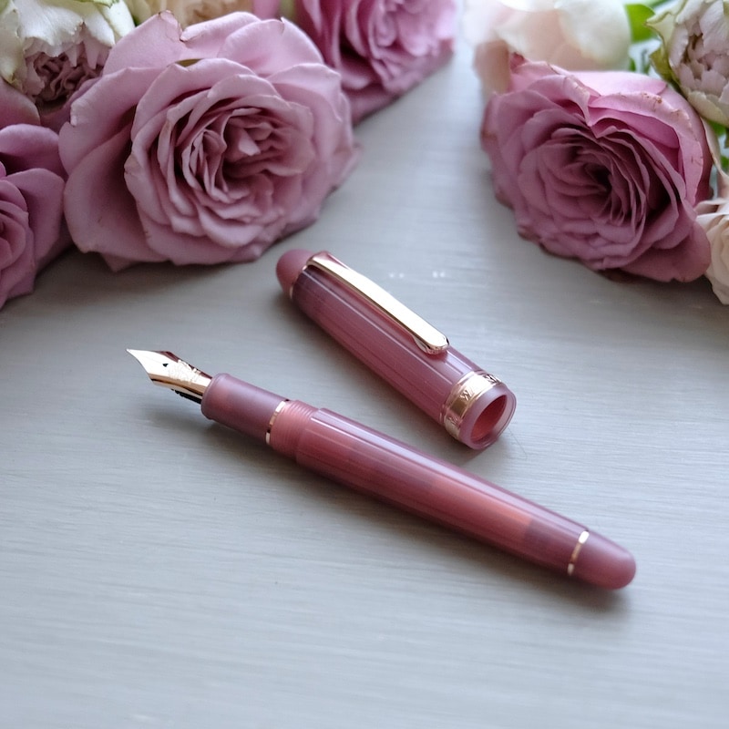 A WAGNER2026 Antique Rose fountain pen with its cap removed is displayed on a light surface next to pink roses.