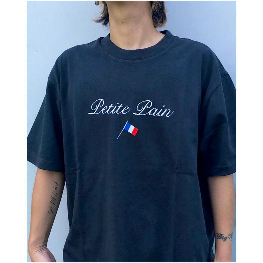 Front view of a black men's cotton t-shirt worn by a model showing the text "Petite Pain" and a small French flag on the chest.
