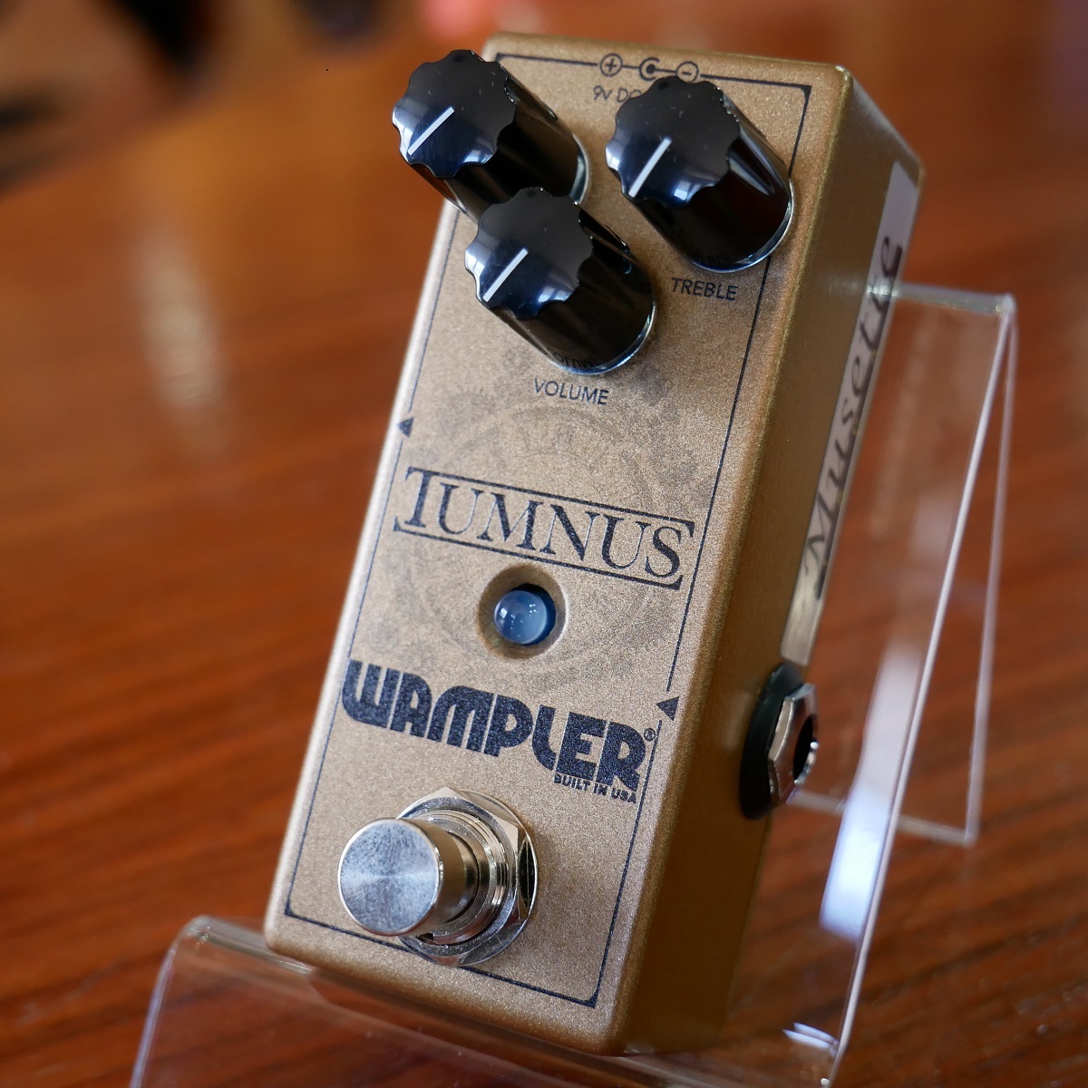 Wampler Tumnus guitar effects pedal with three control knobs, an LED, and a footswitch displayed on a clear stand.