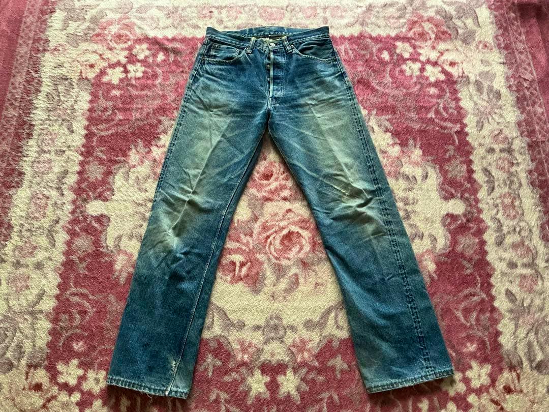 Front view of WAREHOUSE denim jeans laid flat on a patterned rug, showing fading and creases.