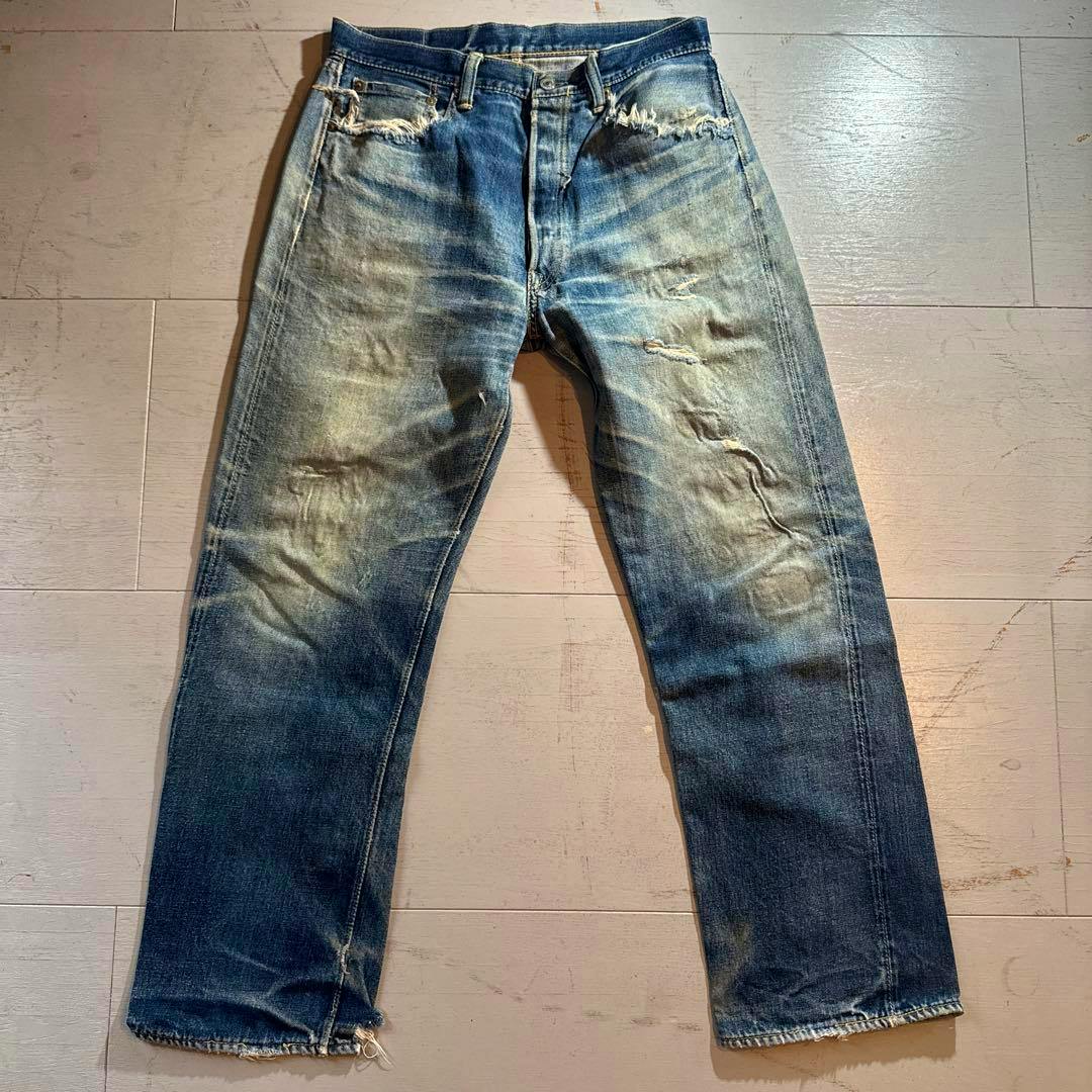 A pair of men's blue cotton jeans laid flat showing fading, distressing, and frayed hems.