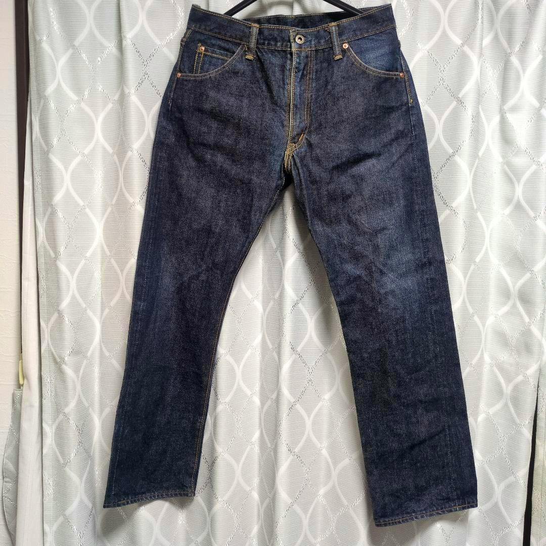 Front view of a pair of dark indigo Lee-model jeans hanging on a hanger against a patterned curtain.
