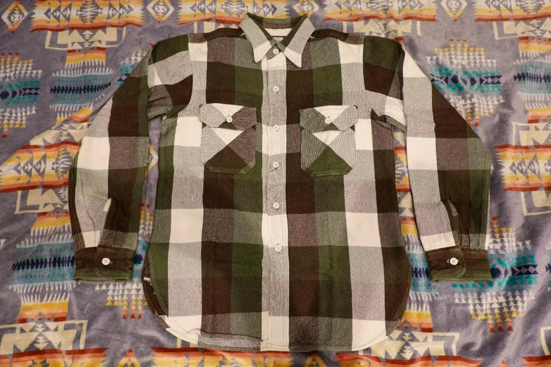 Men's cotton flannel shirt with green, brown, and white large checks laid flat showing the front with buttons and two chest pockets.