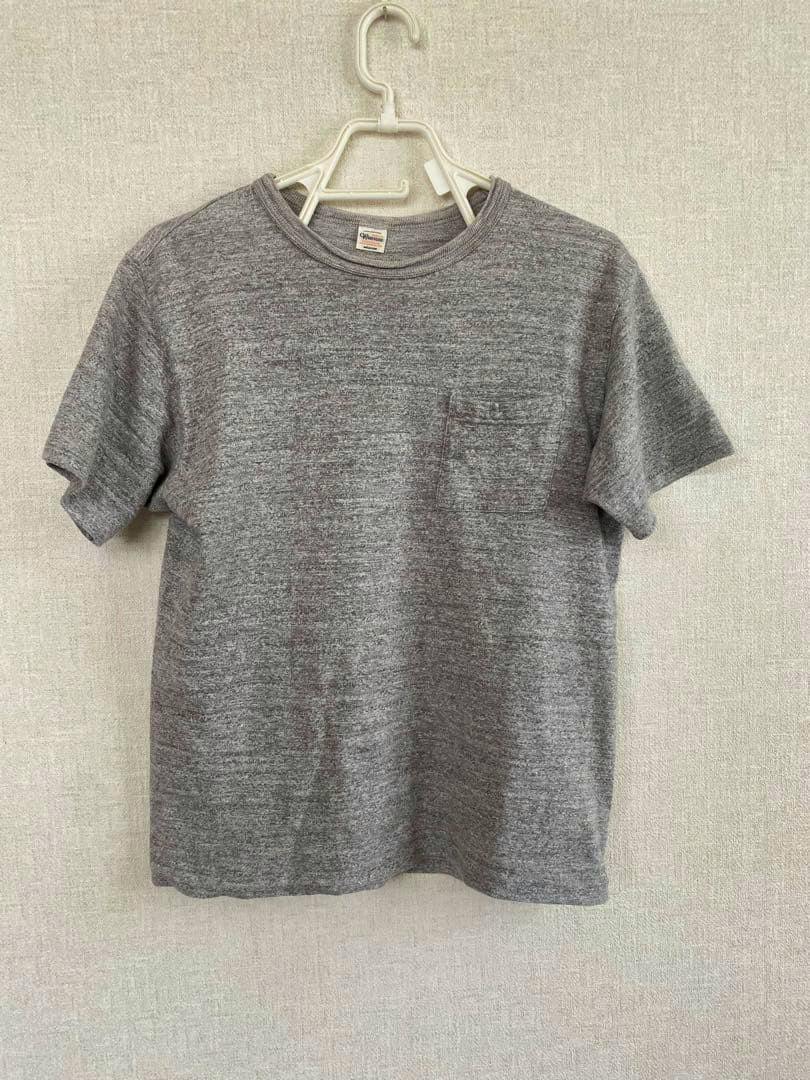 Front view of a gray WAREHOUSE pocket T-shirt hanging on a hanger against a neutral wall.
