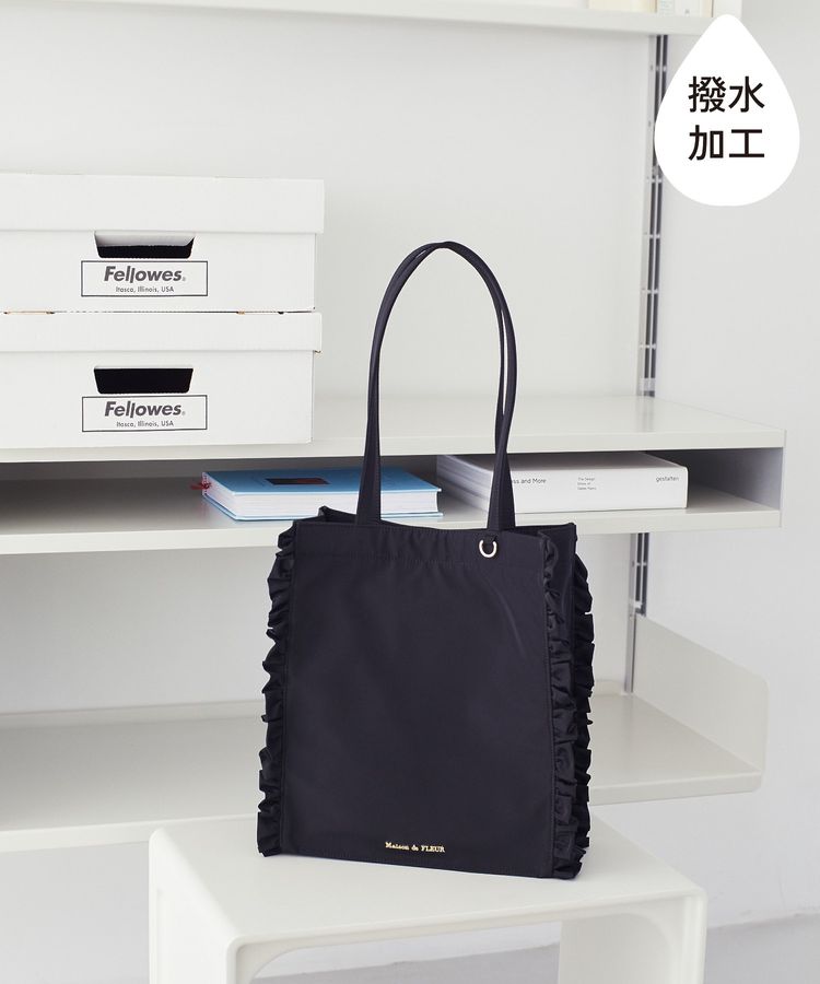 A black square tote bag with side frills and long handles placed on a shelf.