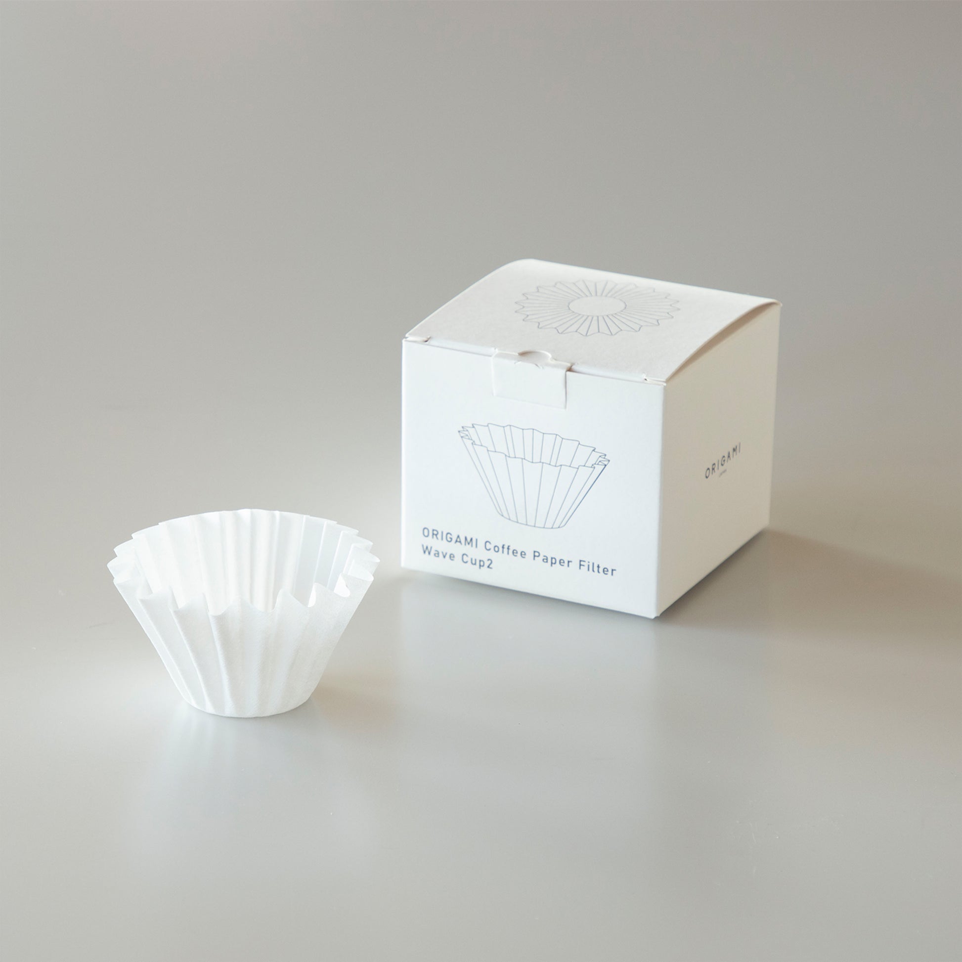 A white wave-style paper coffee filter displayed next to its white packaging box on a neutral surface.