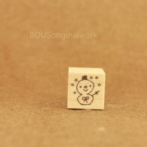 Small wooden weather stamp showing a snowman (snow) design photographed on a brown background.