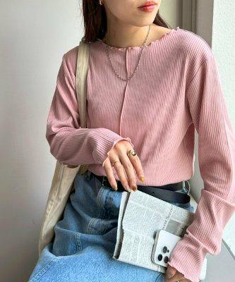 Model wearing a pink polyester ribbed long-sleeve T-shirt shown from the front, seated with jeans and a beige shoulder bag.