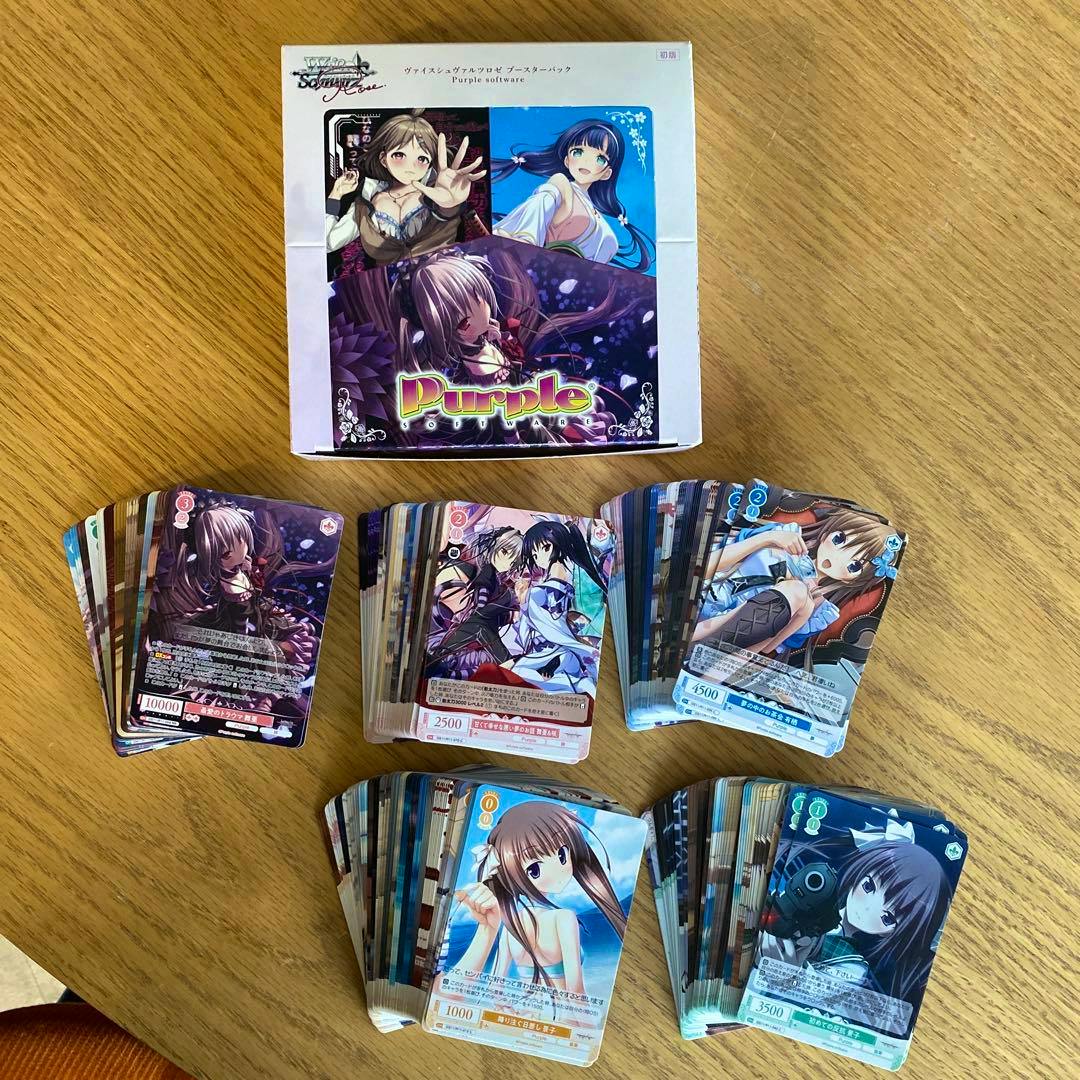 Photo of Weiss Schwarz Purple Software trading cards and a Purple Software booster box arranged on a wooden table.