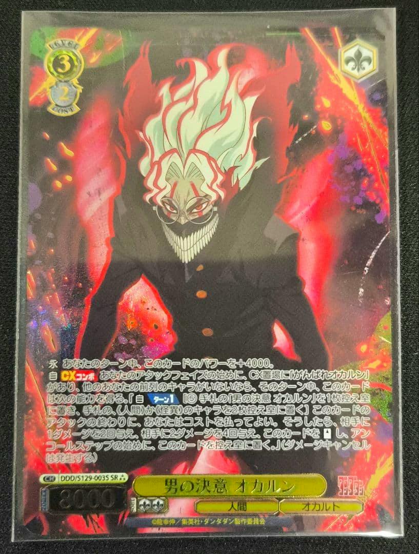 Front photograph of the trading card titled '男の決意 オカルン' showing the illustrated character against a red flaming background with Japanese text.