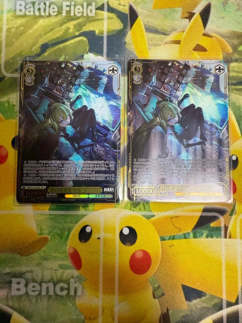 Photo of two Weiss Schwarz trading cards (NIKKE "ラプラス", SR, 3-star) showing the front art placed side-by-side on a Pikachu playmat.