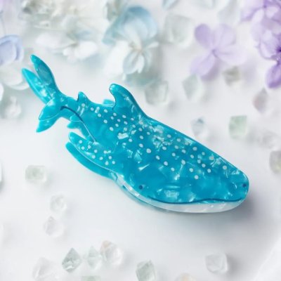 Blue whale shark-shaped hair clip photographed on a light background with decorative stones and flowers.
