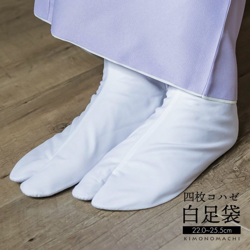White split-toe (tabi) socks being worn on feet under a light purple garment on a wooden floor.