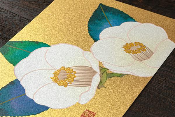 A postcard showing white camellia flowers with green leaves on a gold background.