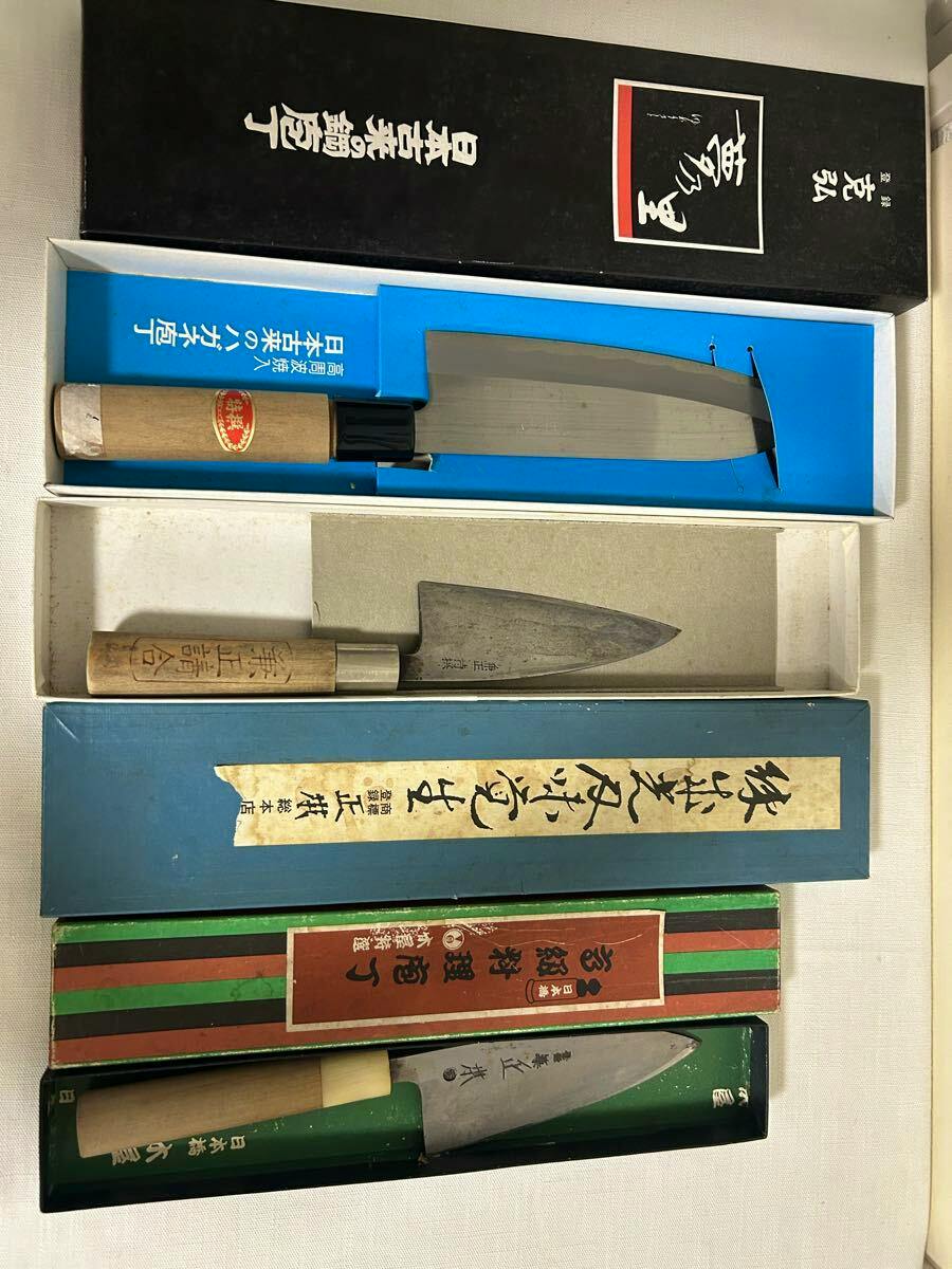 Three kitchen knives in their boxes laid out side by side, showing blades and wooden handles.