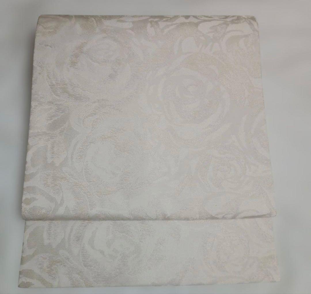 Folded off-white Nagoya obi with an all-over rose pattern displayed on a flat surface.