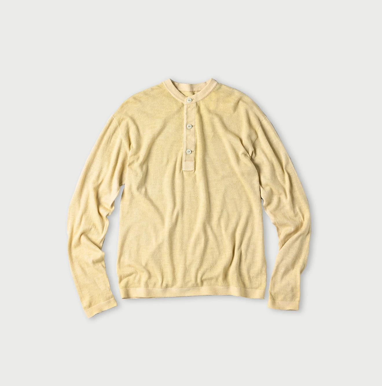 Front view of a light yellow cotton henley sweater laid flat showing a three-button placket.