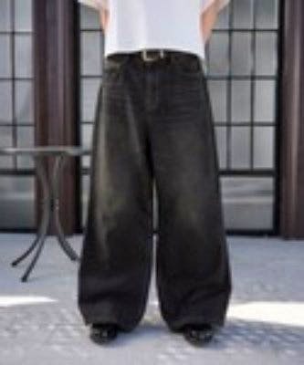Front view of a person wearing wide baggy denim pants shown full-length against a windowed background.