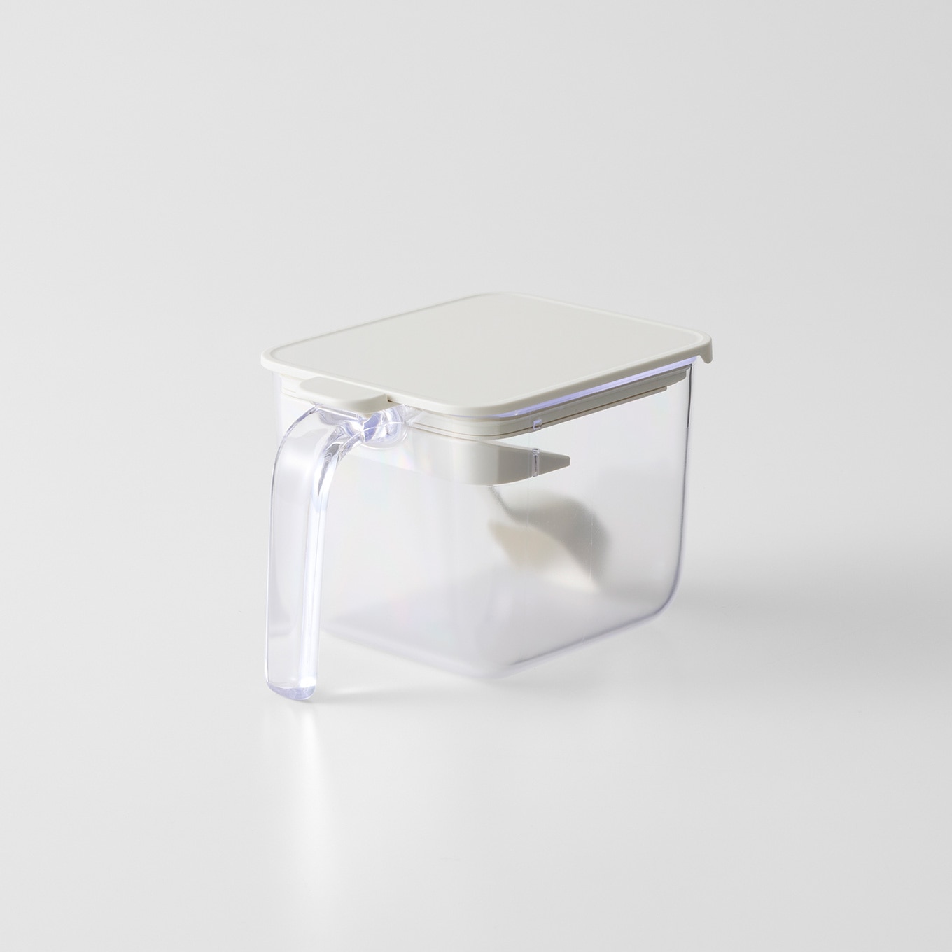 A clear plastic wide seasoning pot with a white lid and a side handle on a white background.