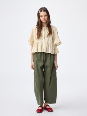 A woman modeling olive-green wide tapered ankle pants paired with a beige top.