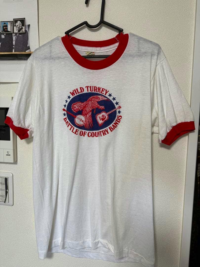 Front of a white ringer T-shirt with red collar and sleeve bands and a centered "WILD TURKEY" "Battle of Country Bands" graphic on the front.